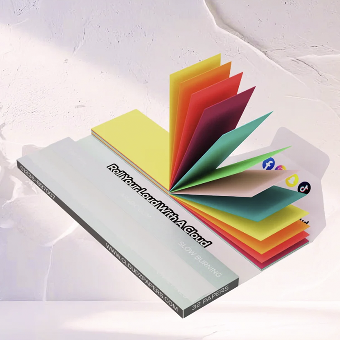 Cloudz-Rolling-Papers-White-1 - Volcano Premium Herbstones Colorful folded paper sheets fanned open from a pale blue rectangular box, resembling a blooming book or flower petals.