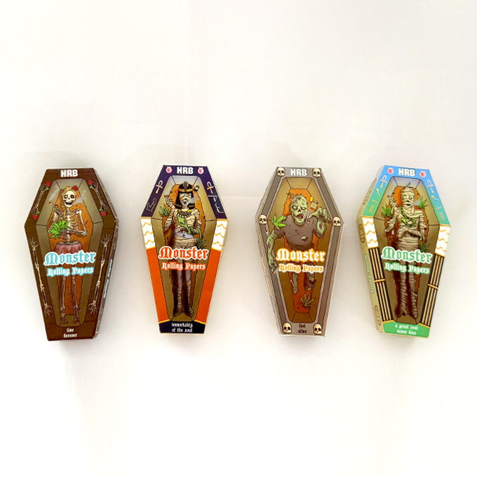 Four coffin-shaped Monster Rolling Papers boxes in brown, orange, gray, and teal, each with a cartoon monster on a white background in a row.