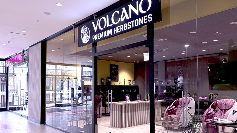 Sind-CBD-Blüten-in-Deutschland-legal Glass storefront with a large illuminated sign reading 'VOLCANO PREMIUM HERBSTONES' in a mall; Burger King sign visible to the left.