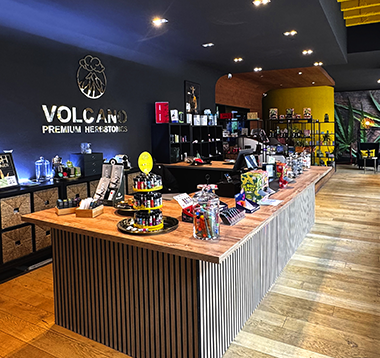 Volcano-Shop-Berlin-Tiergarten-small Bright shop interior with wall-lit display cubes and glass shelves holding cannabis accessories and RAW packaging near a window.